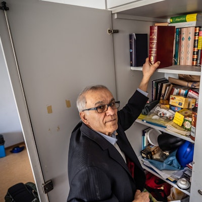 Mahmoud Taghavi steht an einem Schränkchen, in dem Bücher und andere Utensilien seiner Iranischen Gemeinschaft lagern. Bild: Ralf Krieger