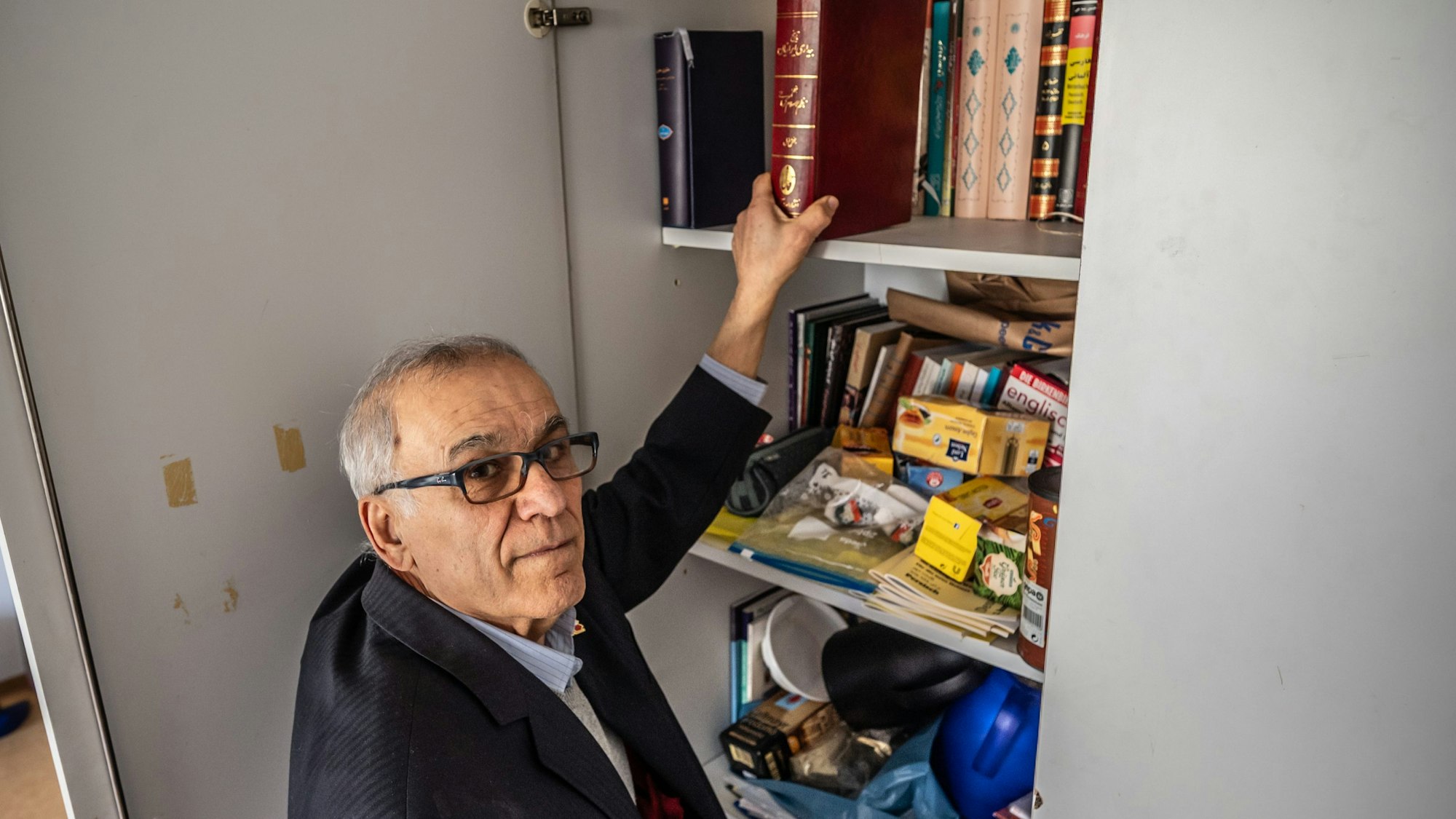 Mahmoud Taghavi steht an einem Schränkchen, in dem Bücher und andere Utensilien seiner Iranischen Gemeinschaft lagern. Bild: Ralf Krieger