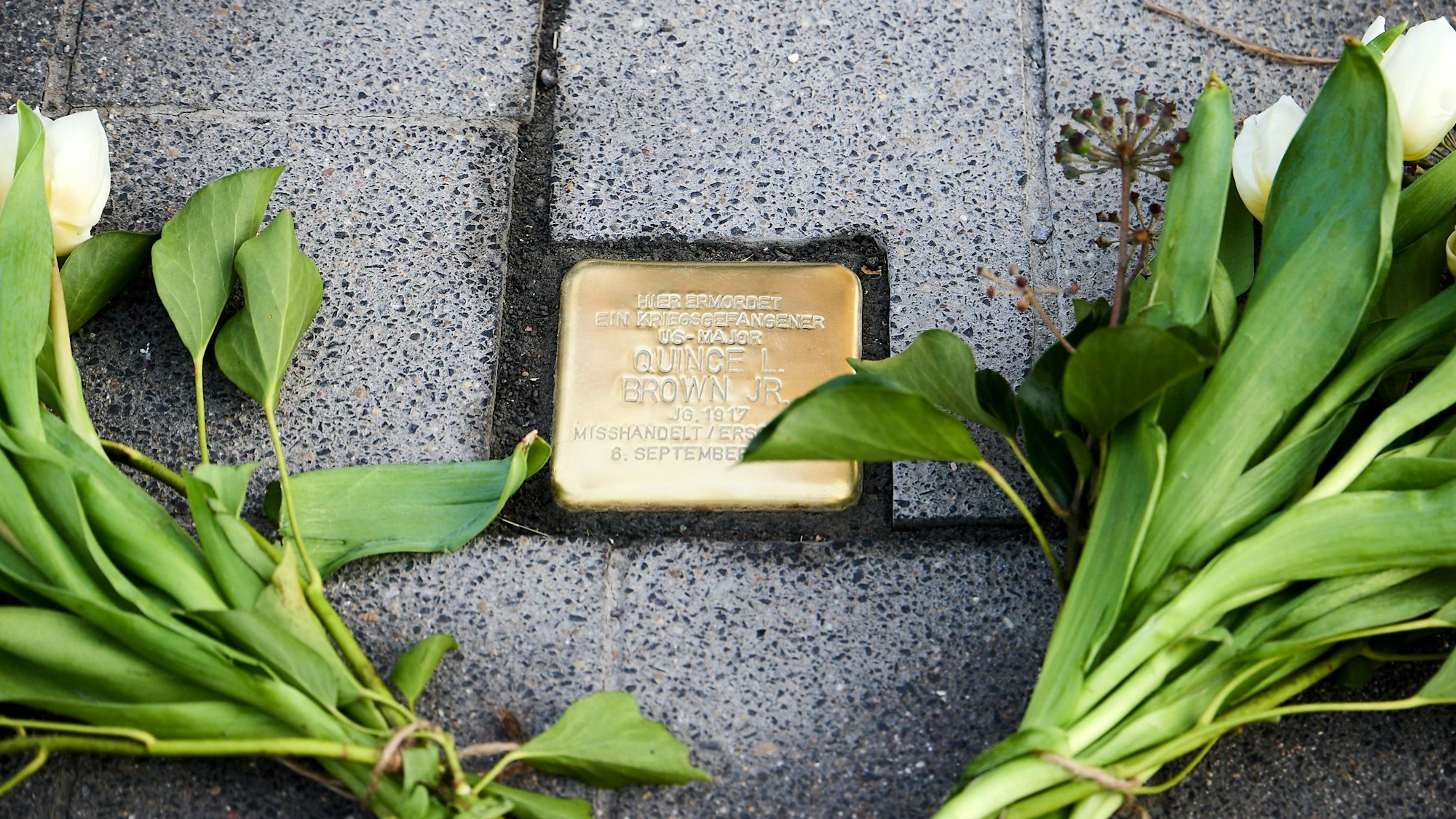 Nahaufnahme des Stolpersteins, der von zwei Blumensträußen flankiert wird
