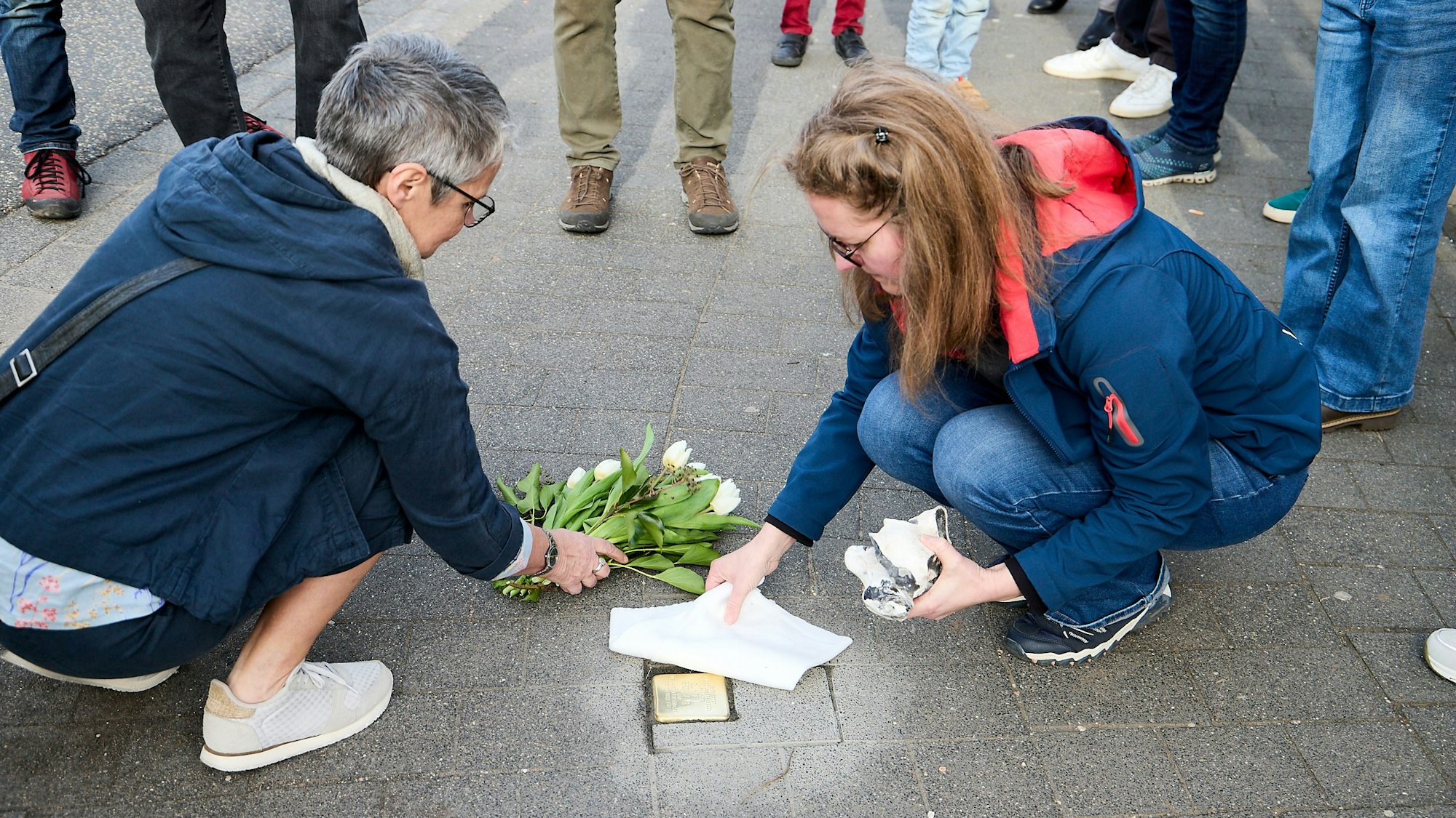 Martina Hilger-Mommer legt einen Strauß Blumen zu dem Stolperstein. Nicole Gutmann zieht eine Abdeckung des Steines ab.