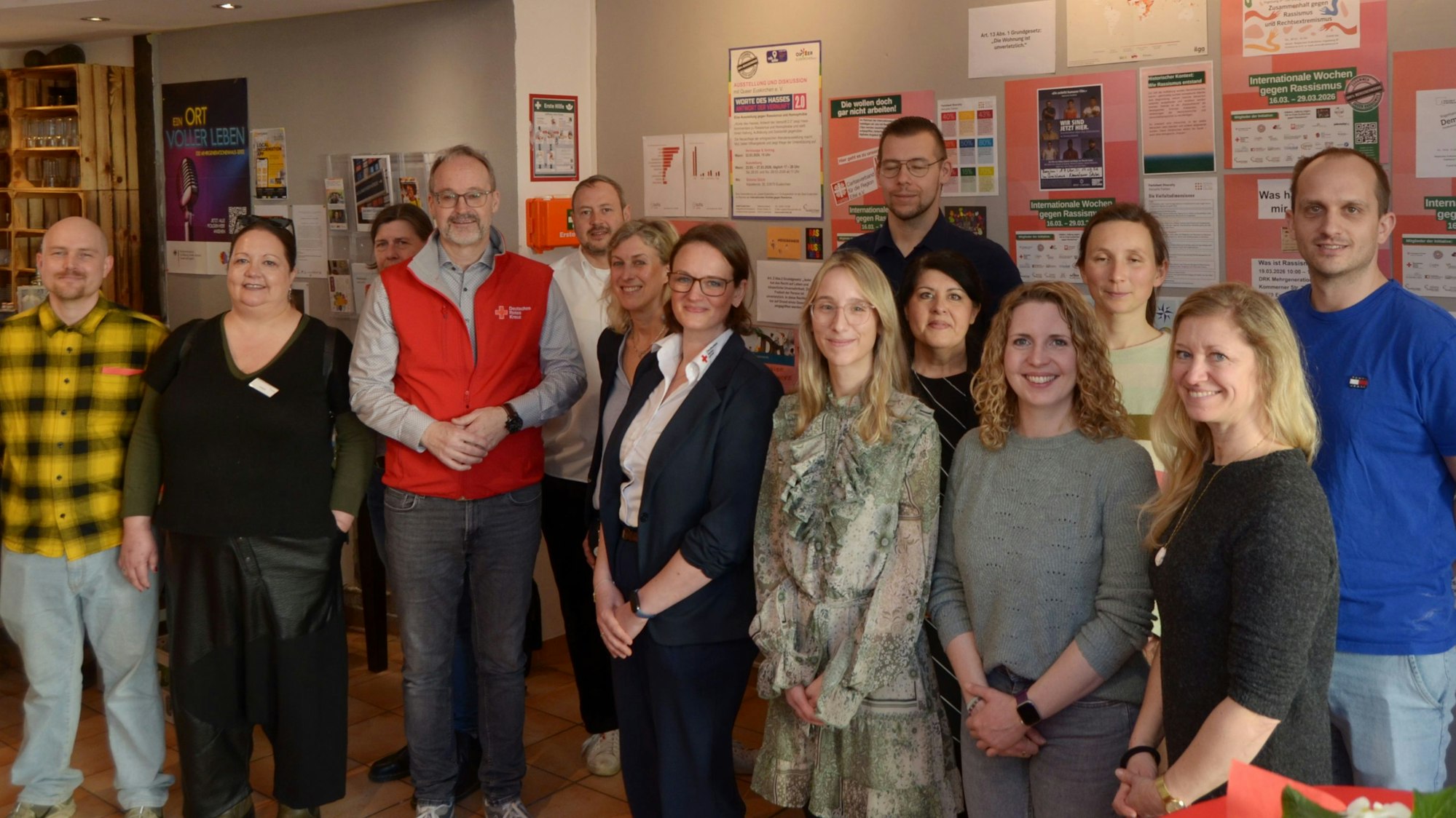 Die Gruppe der oben genannten Vertreter und Vertreterinnen sten vor eine Wand, die mit Plakten gegen Rassismus versehen ist.