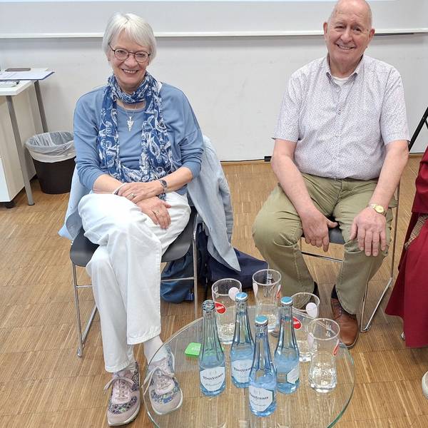 Die drei Obengenannten sitzen auf Stühlen hinter einem Glastisch.