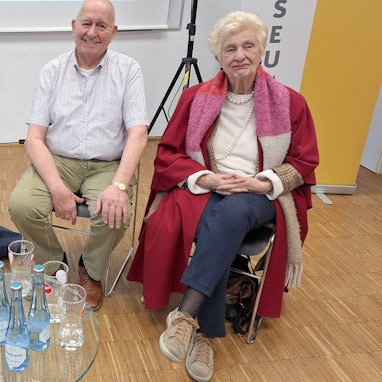 Die drei Obengenannten sitzen auf Stühlen hinter einem Glastisch.