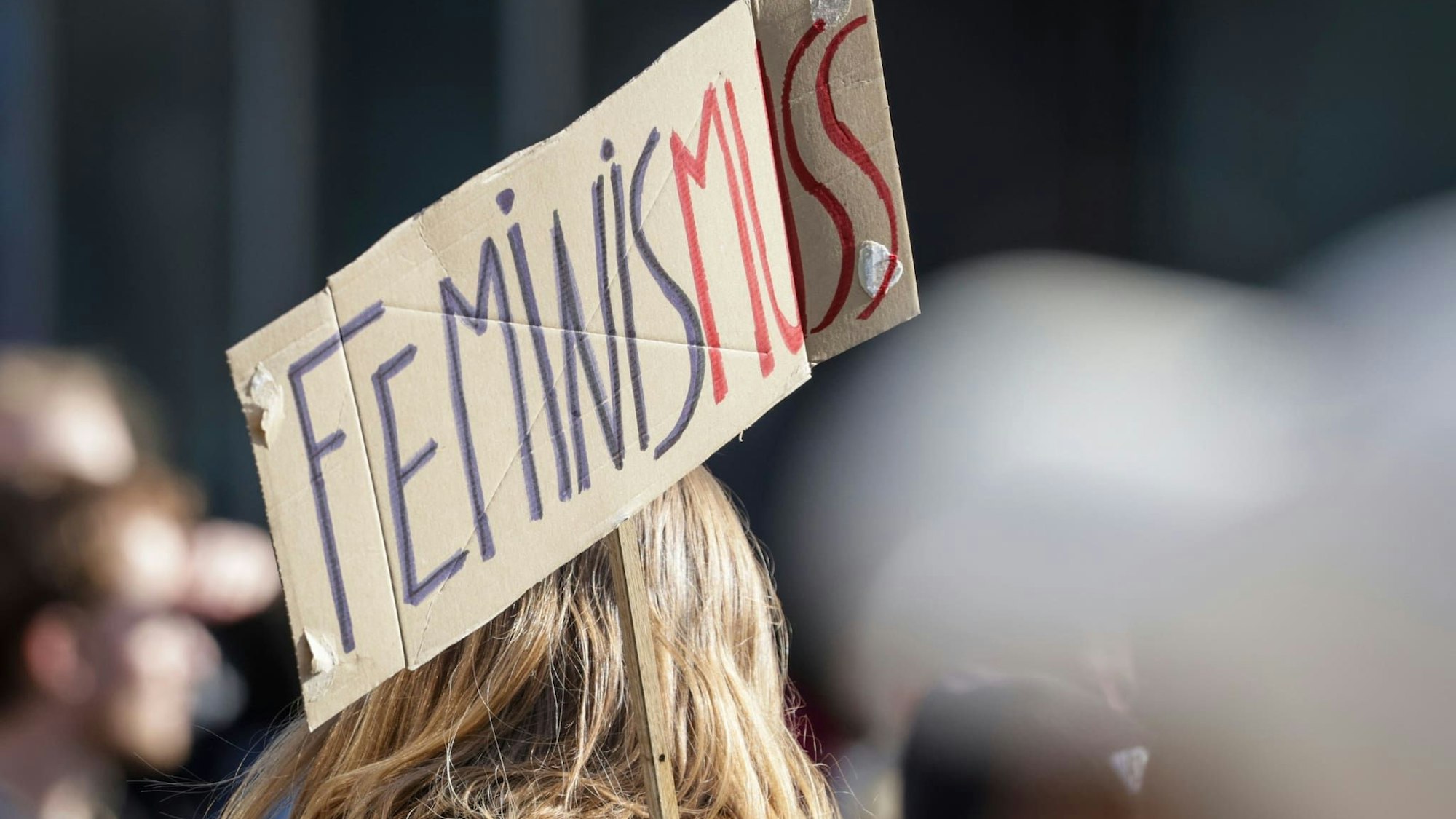 Demo zum Weltfrauentag: Eine Teilnehmerin trägt ein Schild mit der Aufschrift "Feminis-muss".