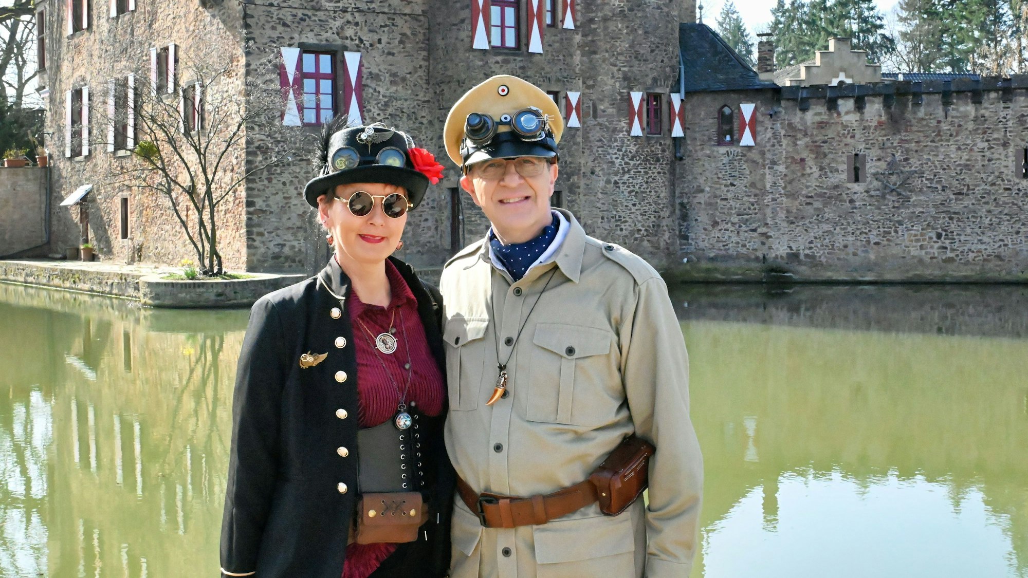 Ein Mann und eine Frau tragen Verkleidungen mit Mänteln und markanten Brillenaufsätzen, die auf ihren Kopfbedeckungen aufliegen.