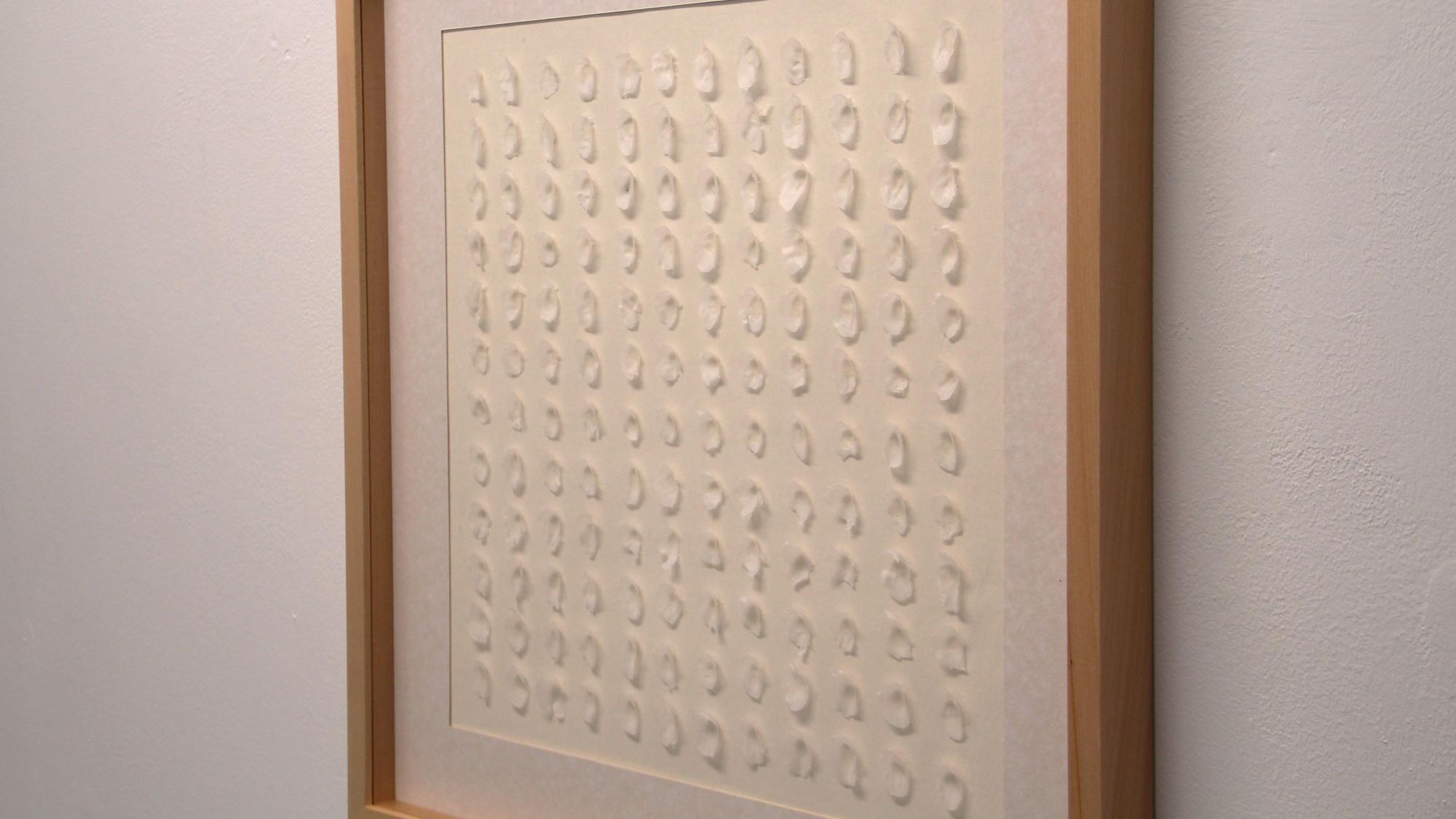 Ein Bild mit weißen Wachsflecken auf weißem Grund hängt an einer Wand.