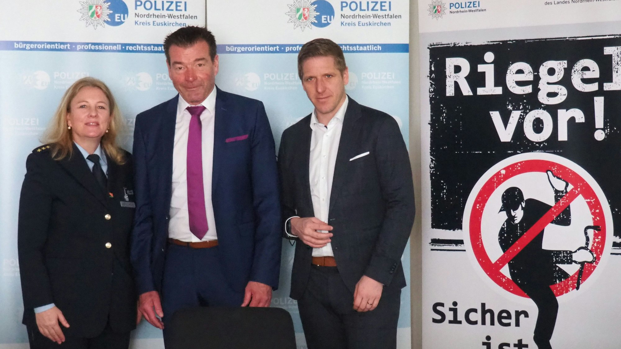 Gabriele Mälchers, Markus Ramers und Ulrich Linden stehen neben einem Plakat, das vor Wohnungseinbrechern warnt.
