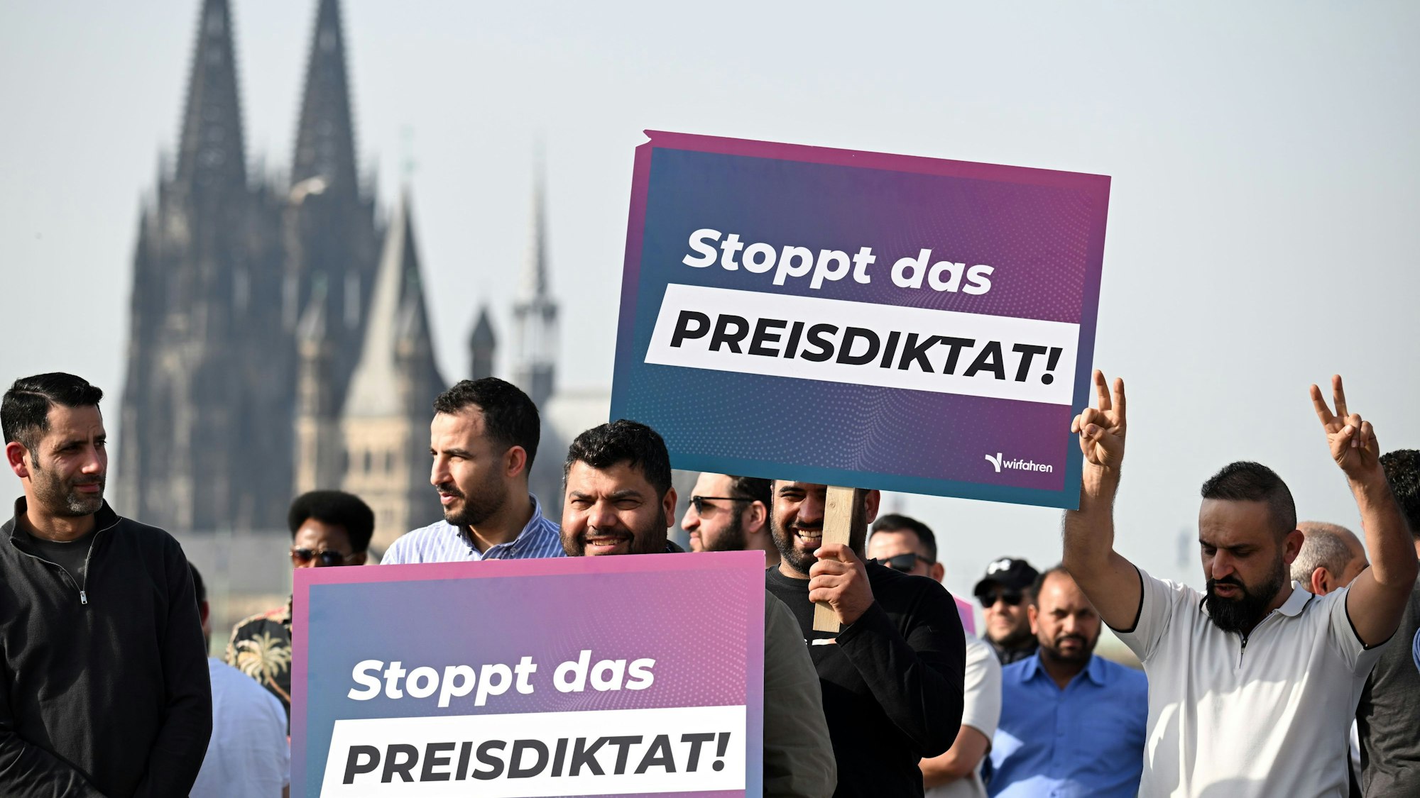 09.03.2026, Nordrhein-Westfalen, Köln: Teilnehmer einer Demonstration halten Schilder mit der Aufschrift „Stoppt das Preisdiktat“ in den Händen. Die Kundgebung richtet sich gegen Pläne der Stadt Köln zur Einführung von Mindestpreisen bei Unternehmen wie Uber und Bolt. Foto: Federico Gambarini/dpa +++ dpa-Bildfunk +++