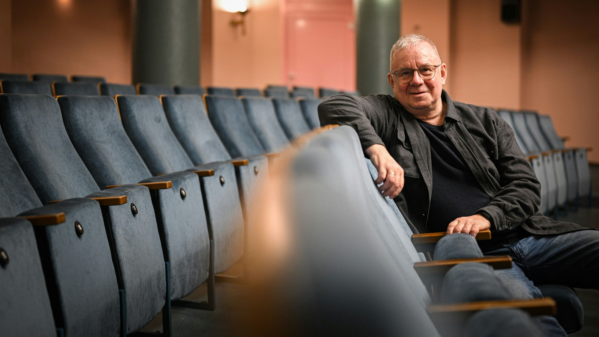 Ein Mann sitzt in einer Stuhlreihe und lächelt in die Kamera.