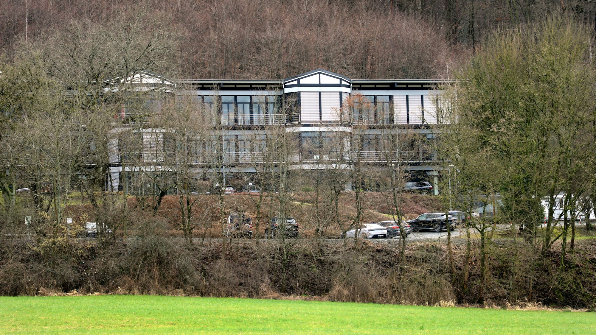 Zu sehen ist ein großes Gebäude hinter Bäumen auf einer Anhöhe.