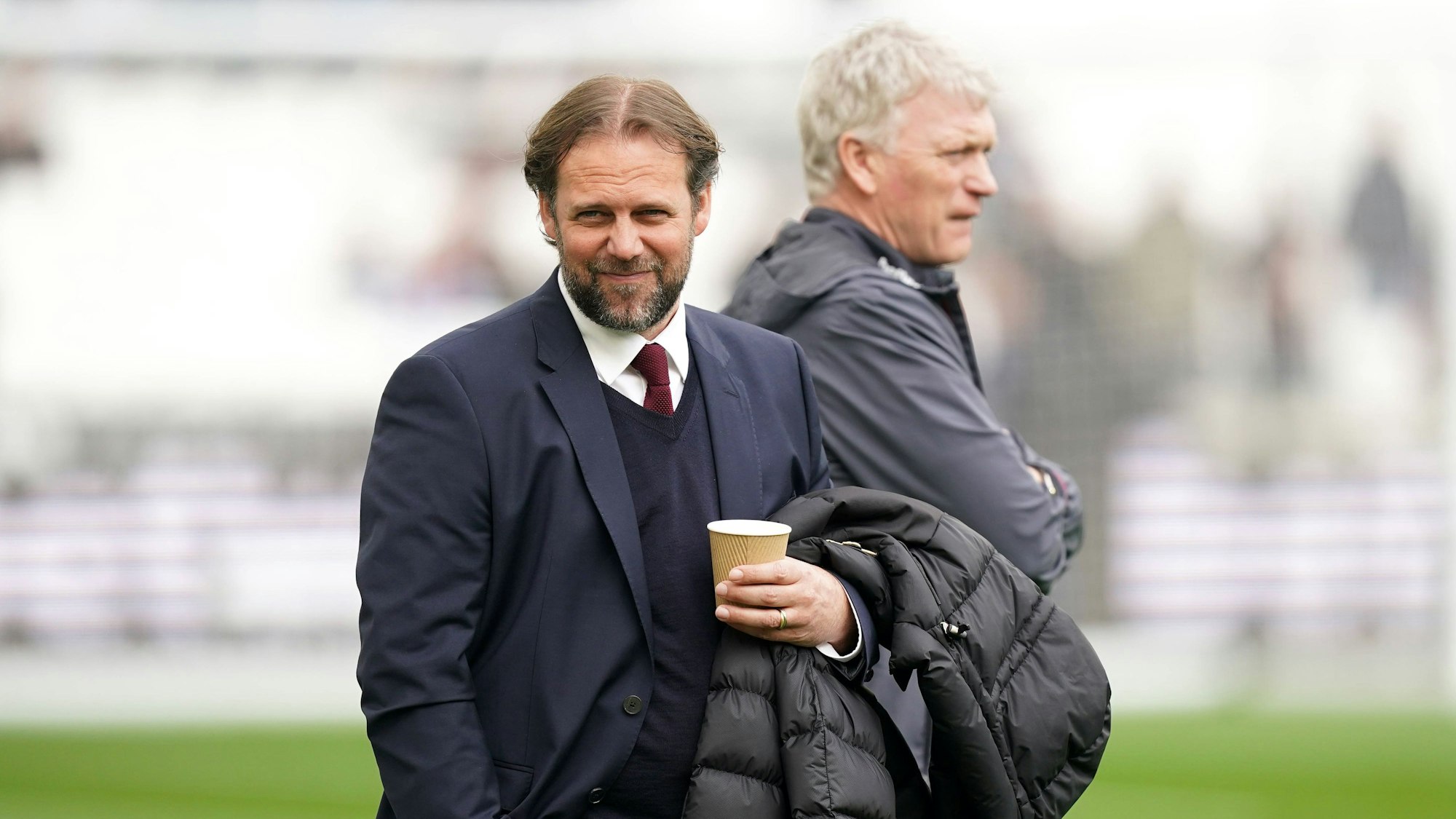 Tim Steidten mit einem Becher in der Hand, im Hintergrund steht Trainer David Moyes.