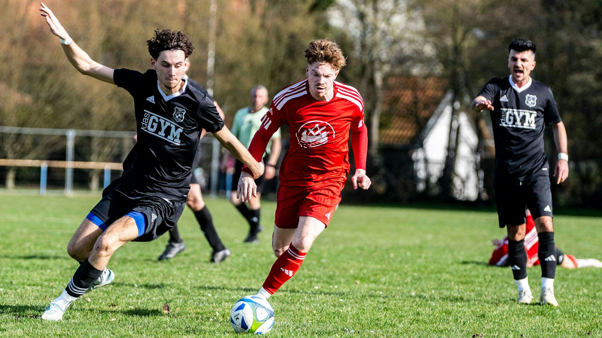 Zwei Fußballer im Kampf um den Ball. Im Hintergrund ruft ein dritter Fußballer etwas.