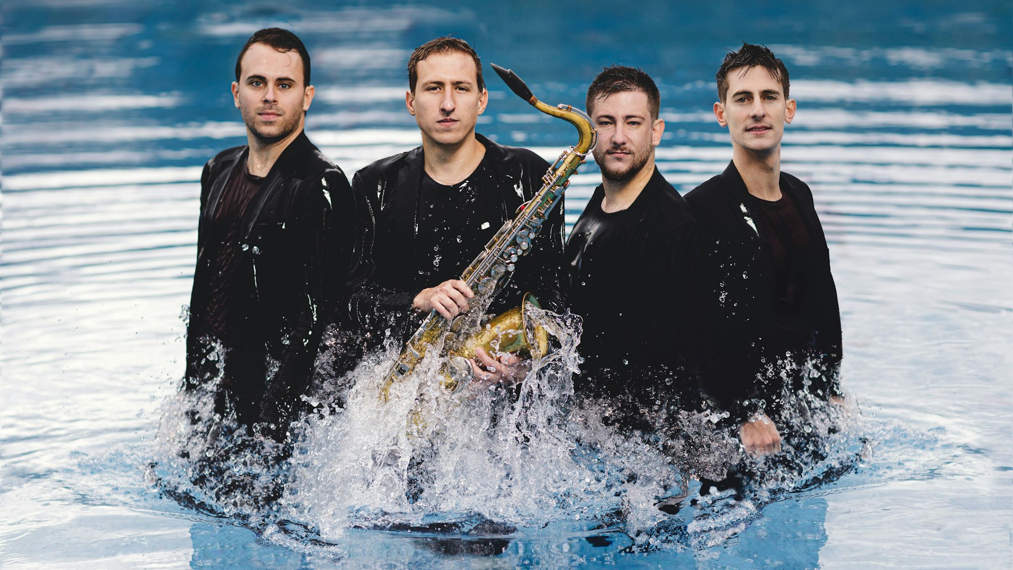 Die vier Musiker stehen schwarz gekleidet im Wasser.