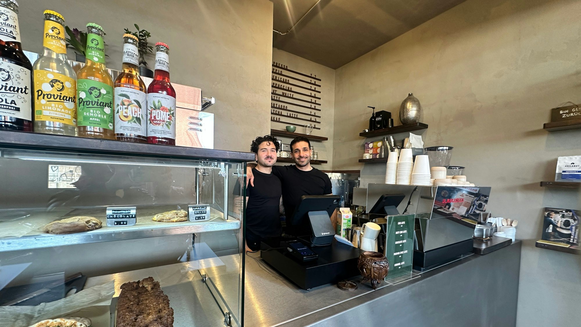 Zwei Männer in schwarzen T-Shirts stehen hinter einem Verkaufstresen.