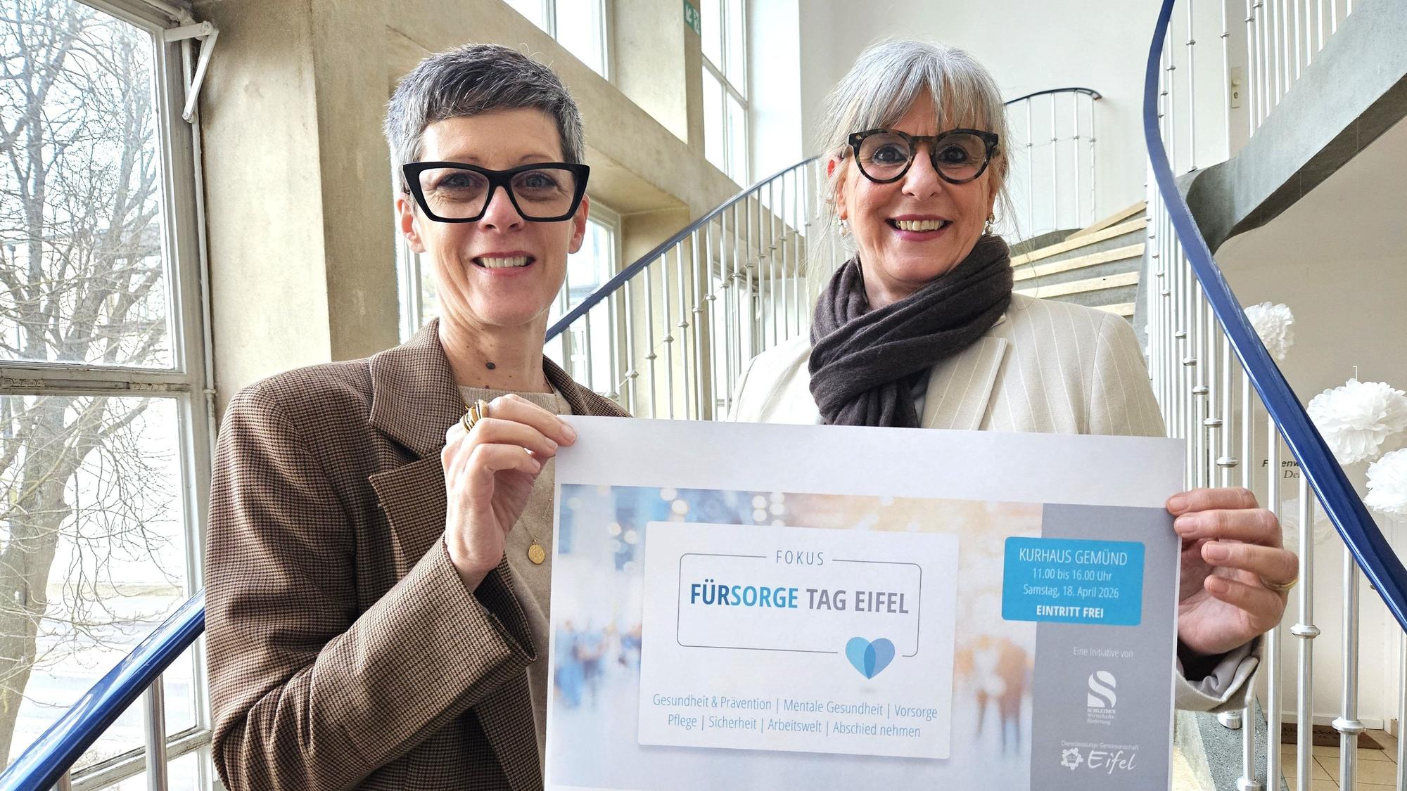 Zwei Frauen stehen nebeneinander und präsentieren ein Plakat vom Fürsorgetag.