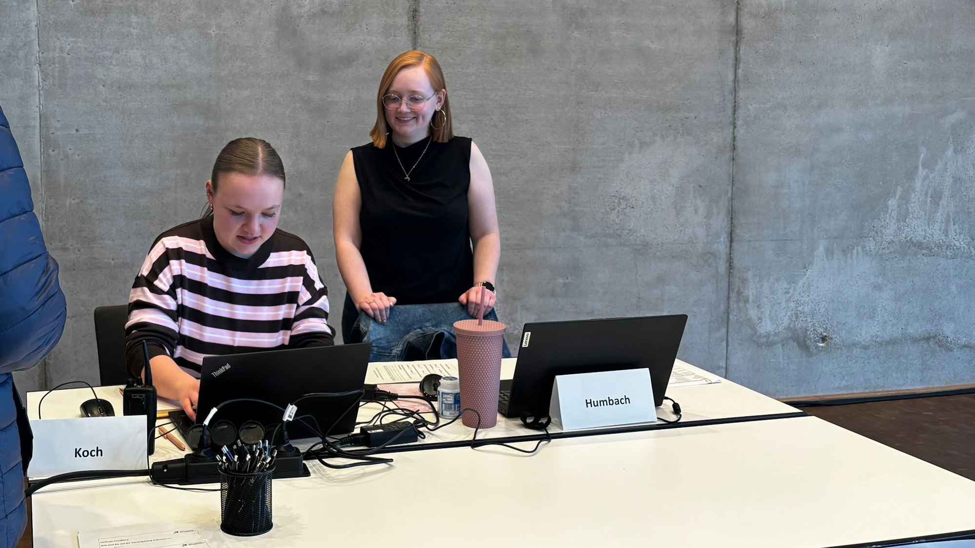 Theresa Koch (l.) sitzt am Tisch und tippt etwas in ihren Laptop. Jasmin Humbach schaut ihr über die Schulter.