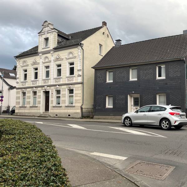 Vor zwei Häusern an der Straße fährt ein Auto vorbei.