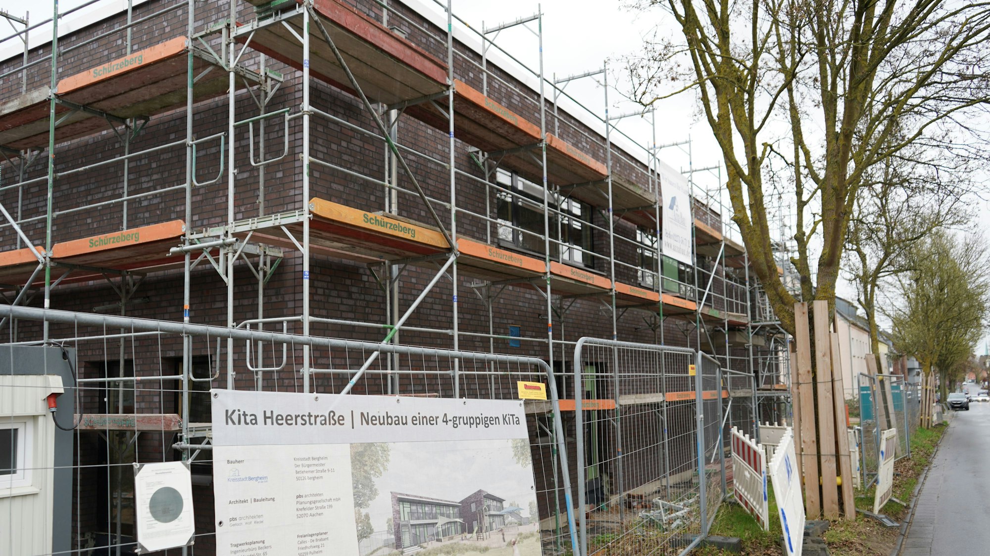 Das Bild zeigt die Baustelle der Kita an der Heerstraße, vor dem Gebäude sind Bauzäune, am Gebäude sind Gerüste zu sehen.