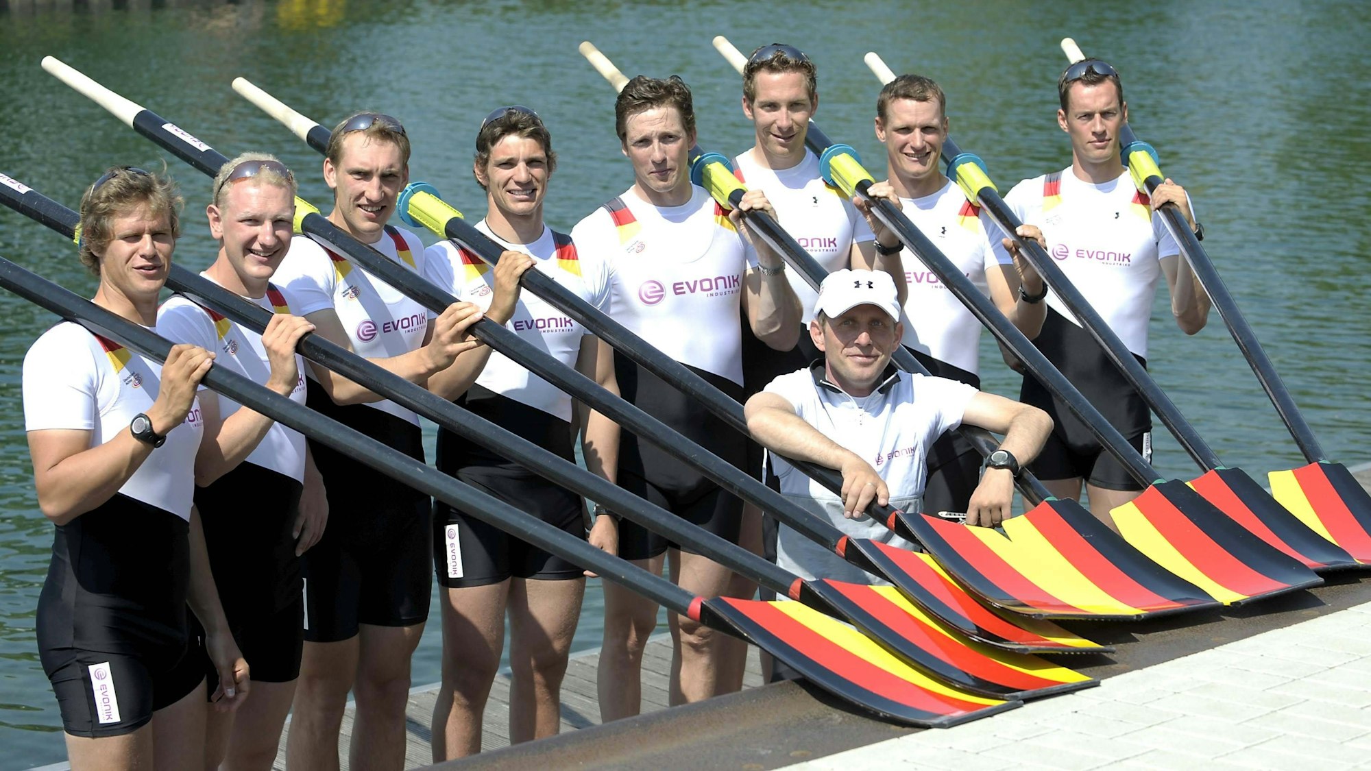 Das Team des Deutschland-Achters steht mit schwarz-rot-goldenen Rudern auf einem Steg, darunter Sebastian Schulte