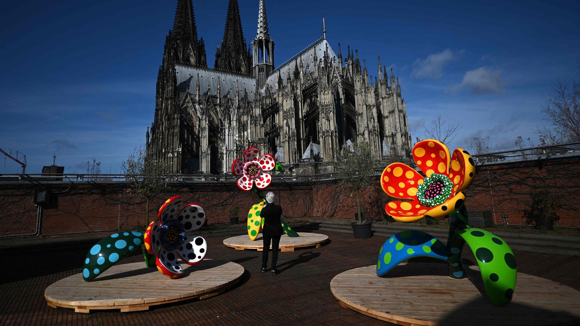 Ein Mann fotografiert eine Blumenskulptur vor dem Hintergrund des Kölner Doms.