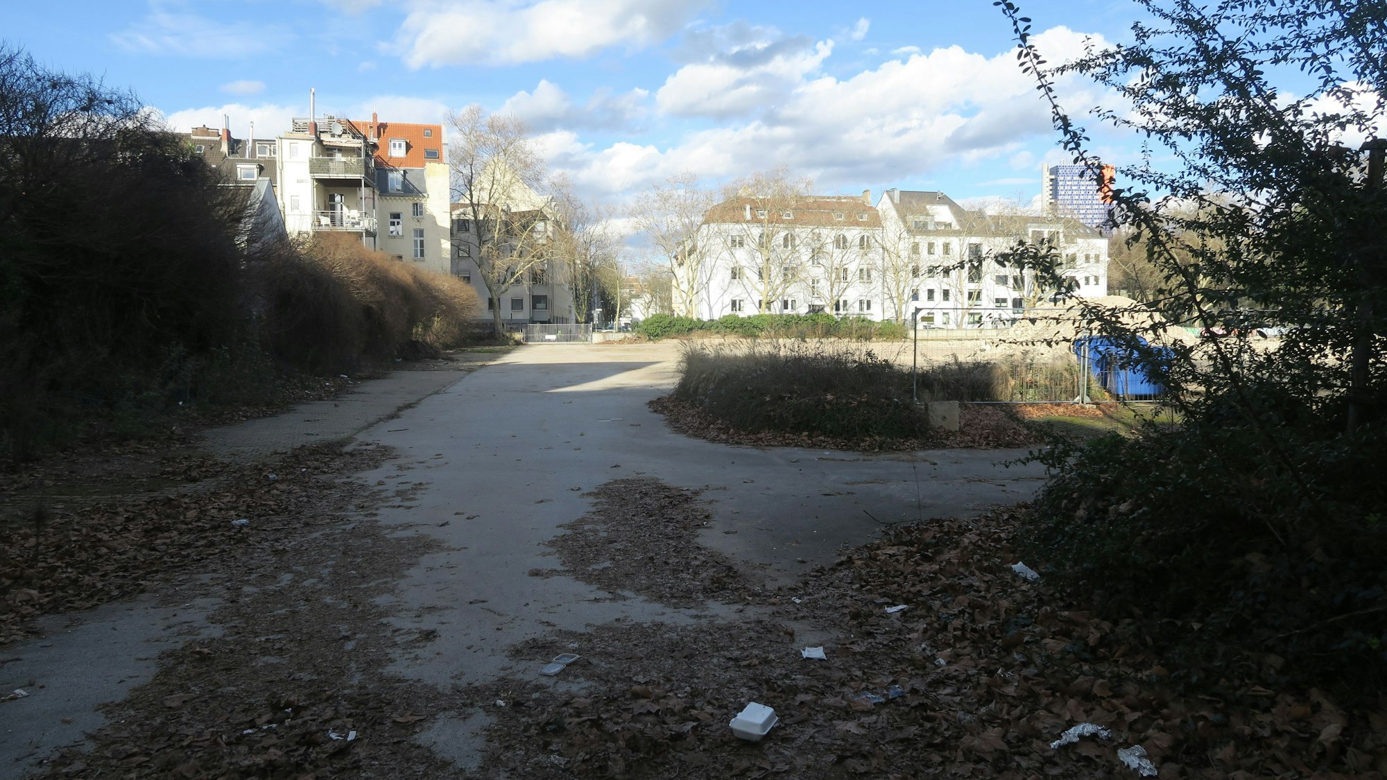 Hinter einer Brachfläche ist Wohnbebauung zu sehen.