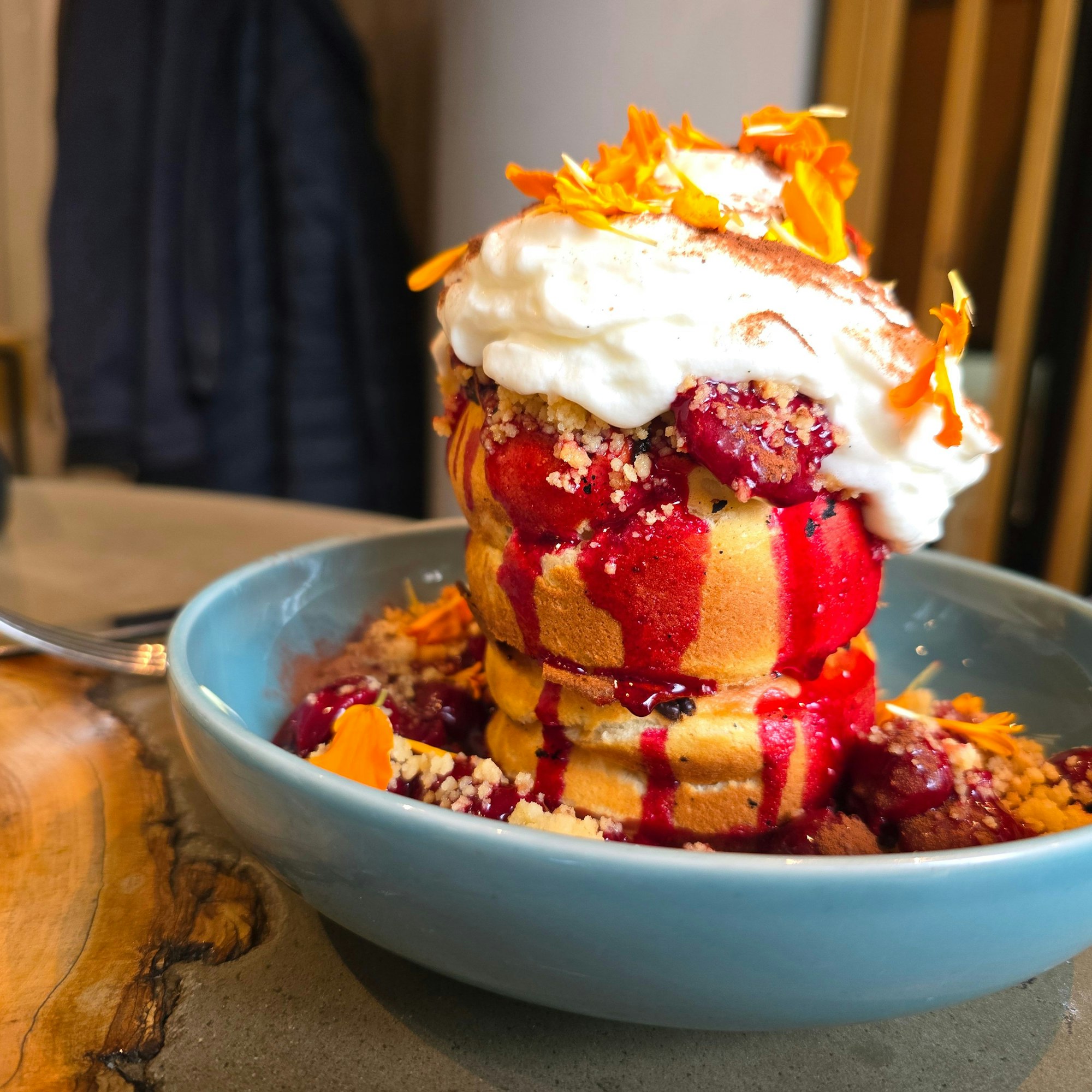 Ein Stapel dicker Pancakes unter Sahne und Kirschen ist auf einem Teller zu sehen.
