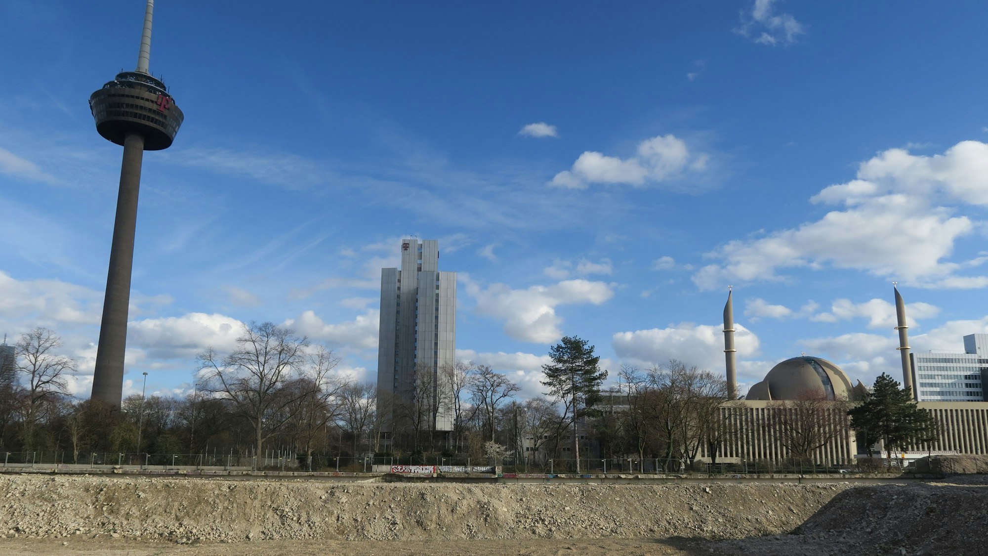 Hinter einer Brachfläche sind der Fernsehturm, ein Bürohochhaus und eine Moschee zu sehen.