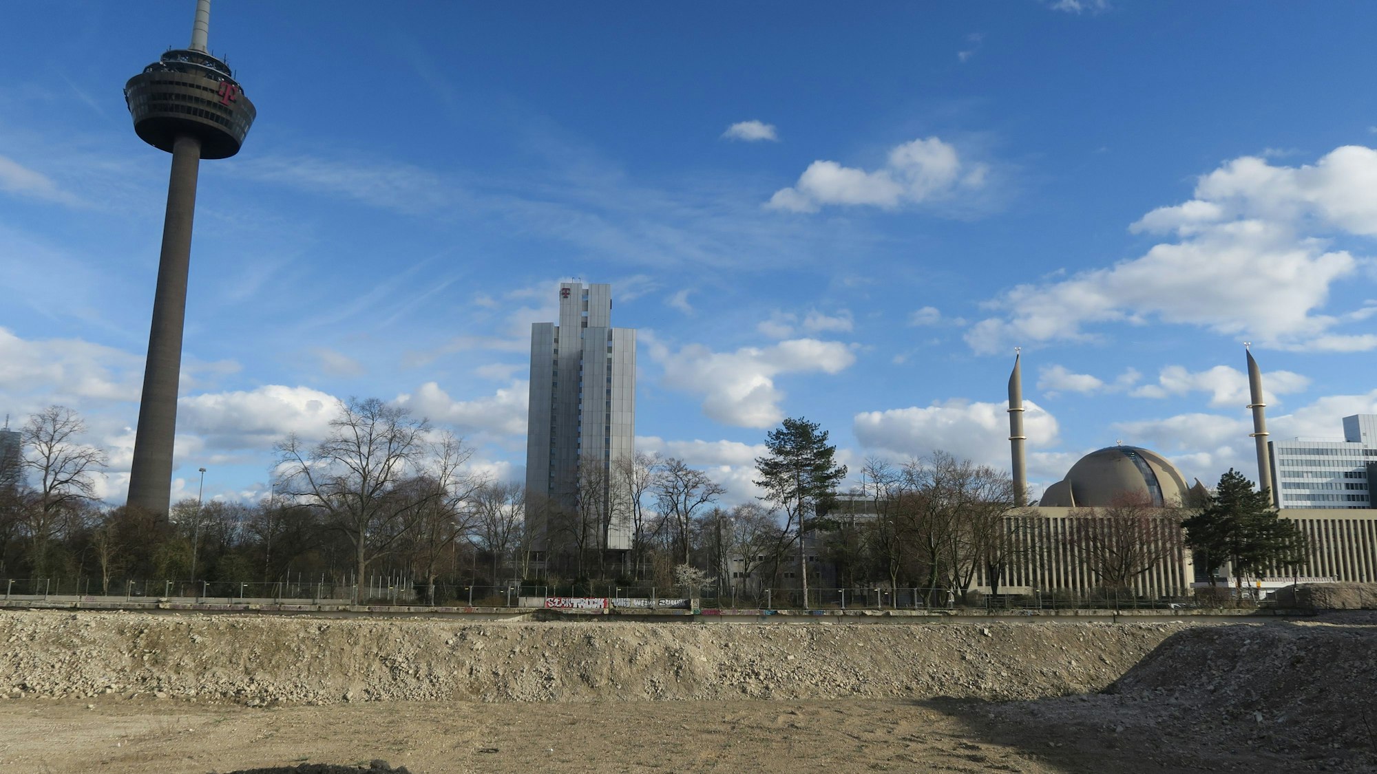 Hinter einem Baugrundstück ragen der Colonius, ein Telekom-Hochhaus und die Moschee in die Höhe.