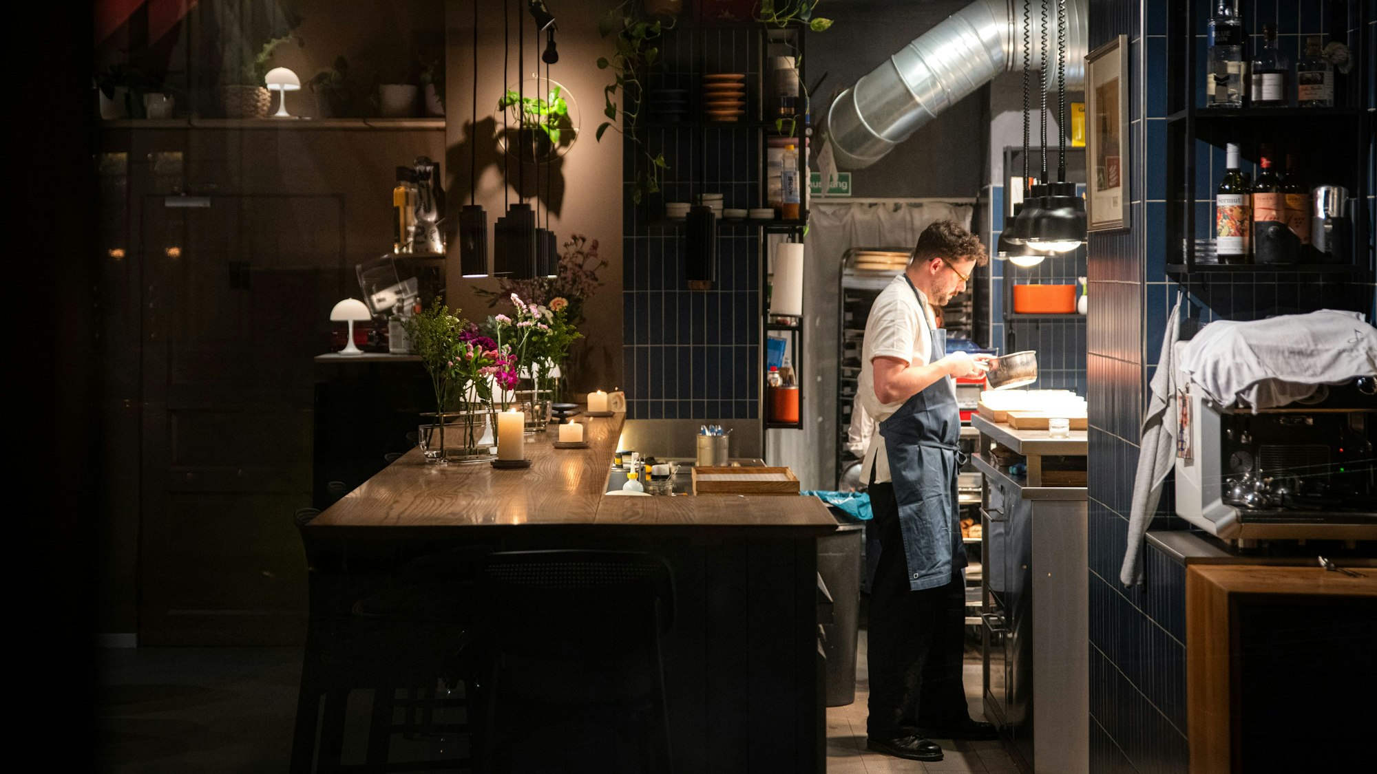 Ein Ausschnitt des Gastraums und der Küche ist zu sehen. Herr Sablotny steht dort und hantiert.