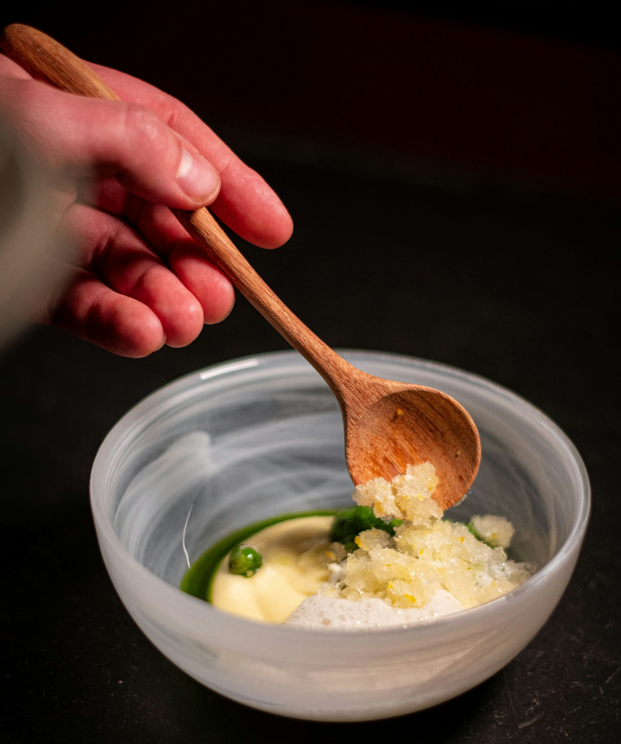 Ein Schälchen zeigt Kartoffelpüree umgeben von grüner Emulsion. Mit einem Holzlöffel wird Granité aufgelöffelt.