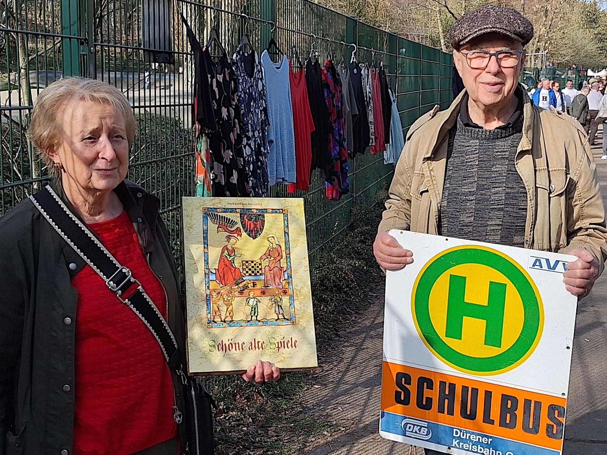 Eine Frau und ein Mann halten ein Schild und eine Spielekiste in die Kamera.