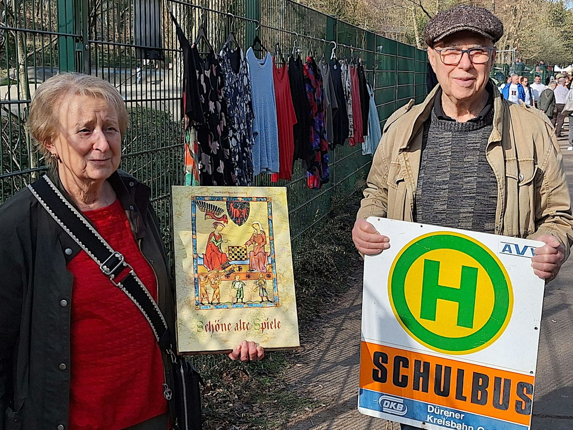 Eine Frau und ein Mann halten ein Schild und eine Spielekiste in die Kamera.