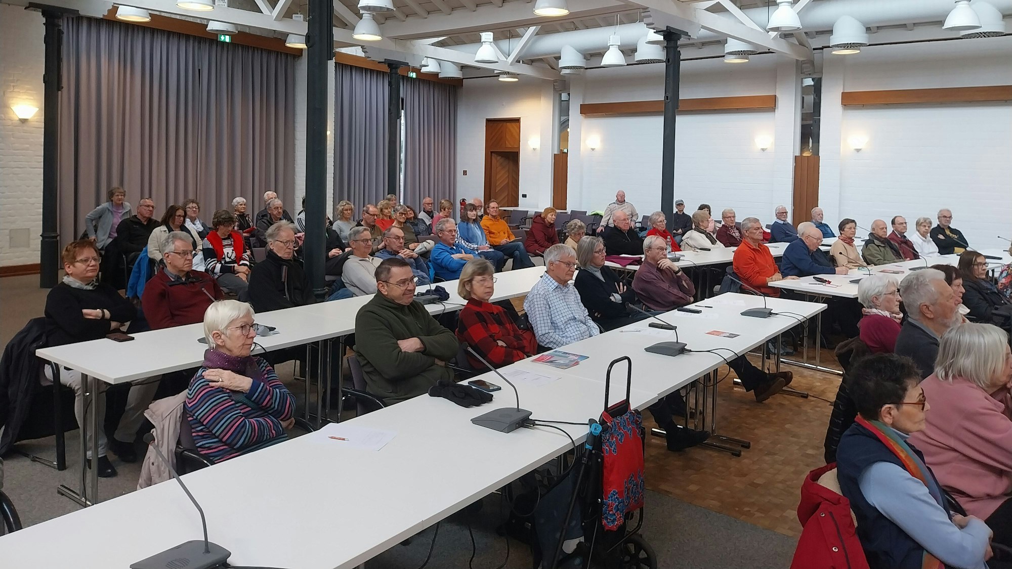 Menschen sitzen an weißen Tischen und blicken aufmerksam nach vorne.