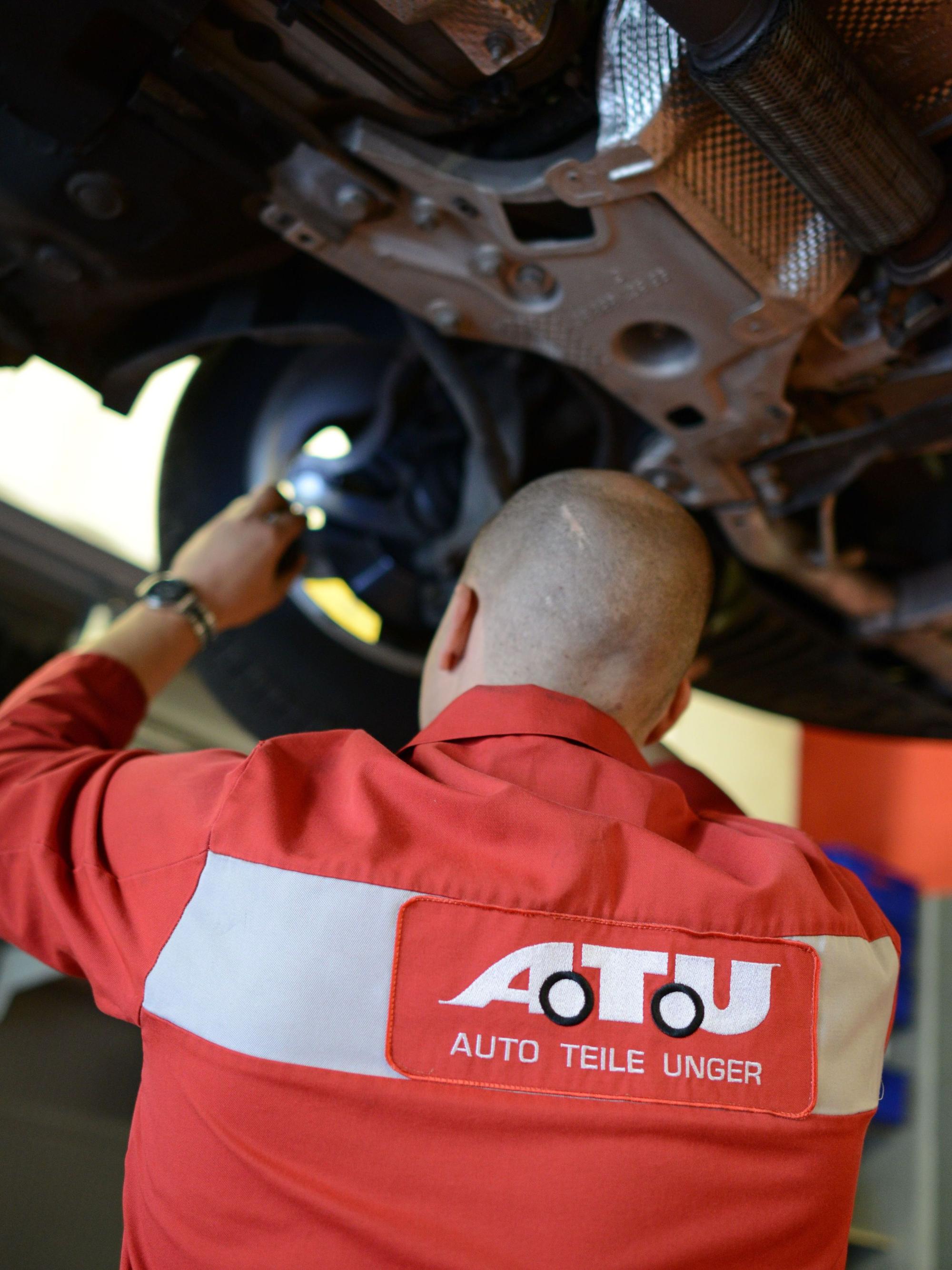 Ein Mitarbeiter der Werkstattkette ATU inspiziert ein Auto, das auf einer Hebebühne steht.