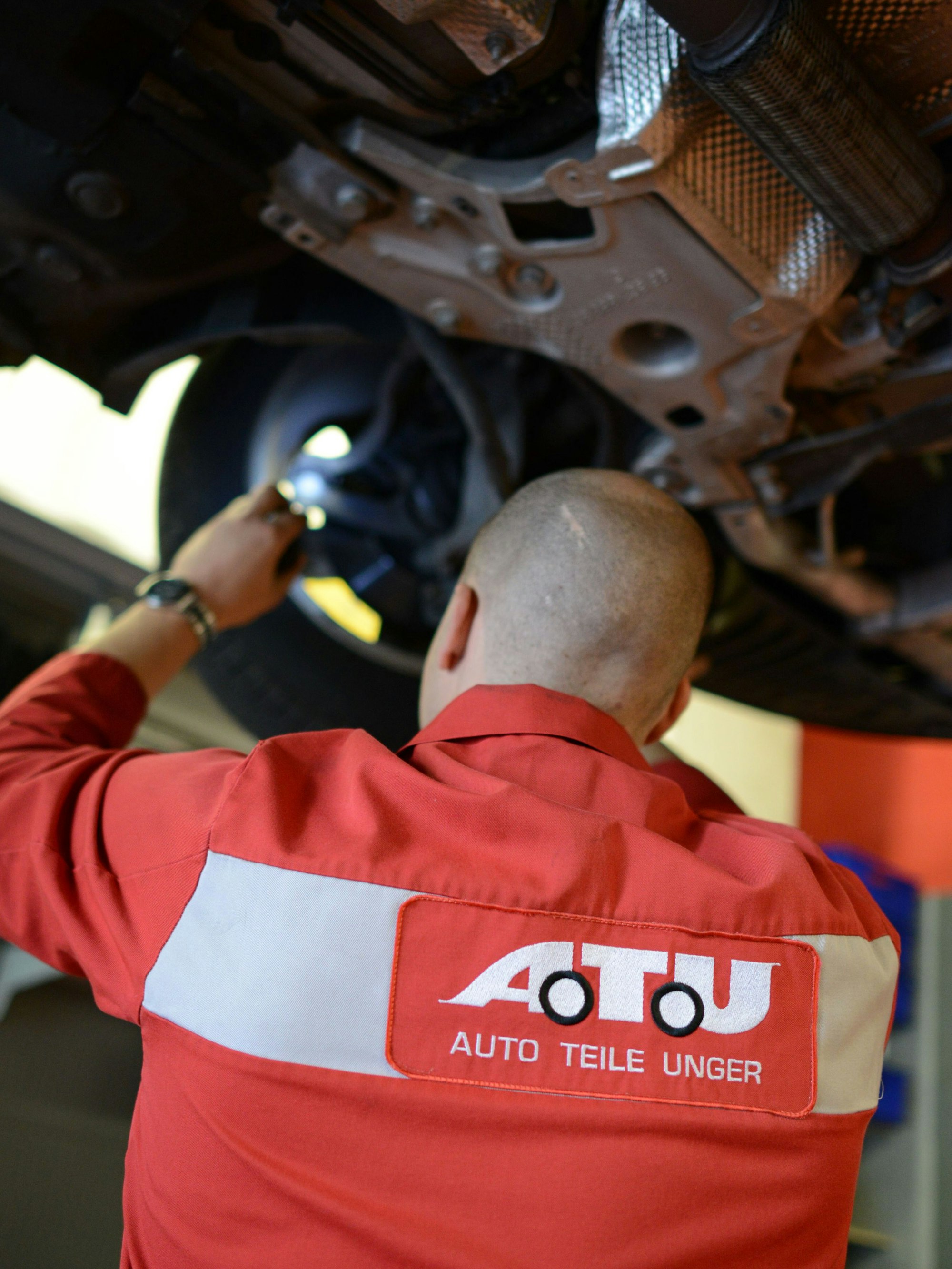 Ein Mitarbeiter der Werkstattkette ATU inspiziert ein Auto, das auf einer Hebebühne steht.