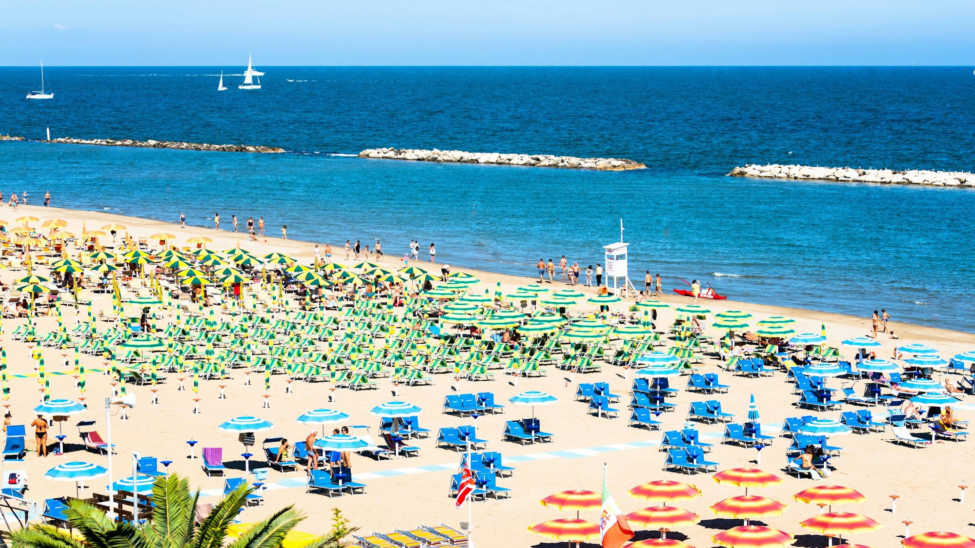 Menschen ruhen sich an einem Sommertag in Rimini am Strand, am Meer und auf Liegestühlen mit Sonnenschirmen aus.