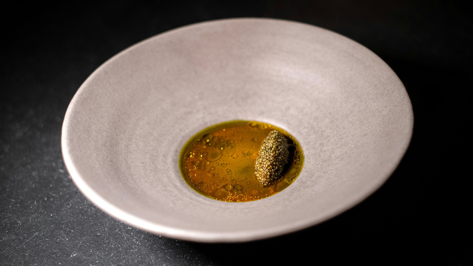 Ein hellgrauer Teller ist zu sehen, mit einem Spiegel aus Sauce und Öl, darauf eine Nocke aus Tonburi.