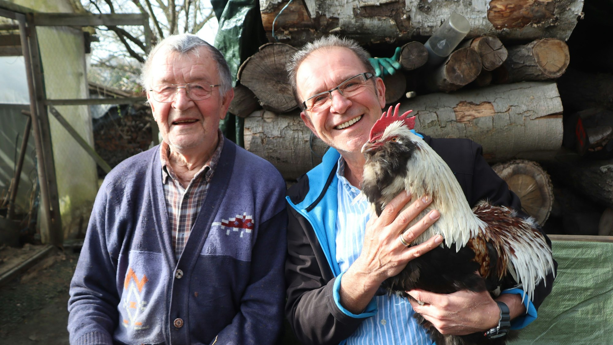 Das Foto zeigt die beiden Männer mit einem Hahn auf der Bank im Schrebergarten.