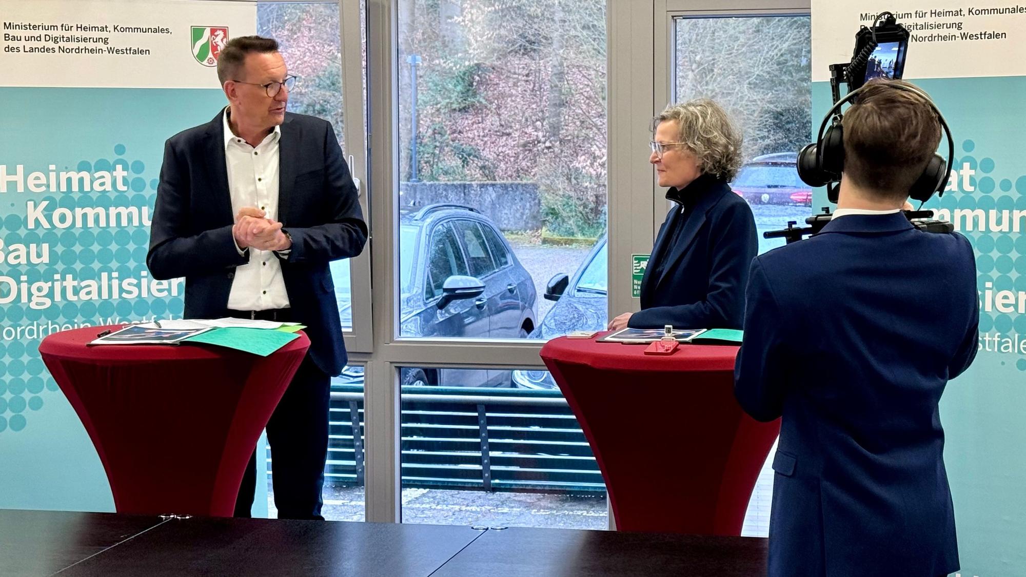 Dirk Runge und Ina Scharrenbach werden von einem Medienmitarbeiter des Ministeriums gefilmt.