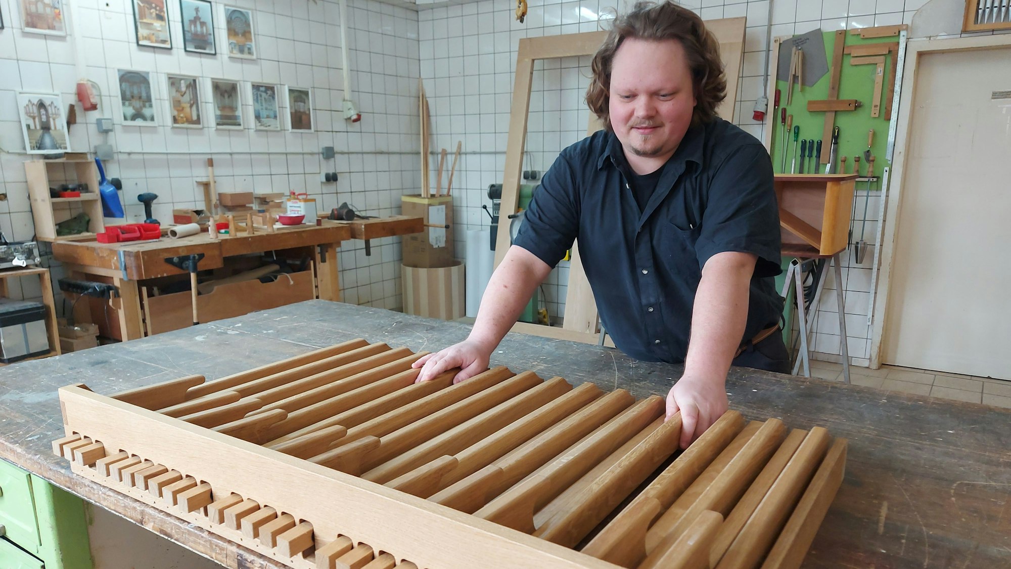 Ein Mann steht in einer Werkstatt an einem großen Lattenrost aus hellem Holz.