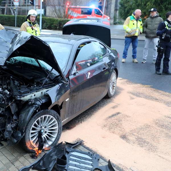 Feuerwehrleute stehen um ein schwer beschädigtes Auto in Bergisch Gladbach-Sand.