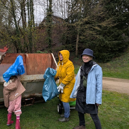 Zwei Erwachsene und zwei Kinder werfen Müll in einen Container.