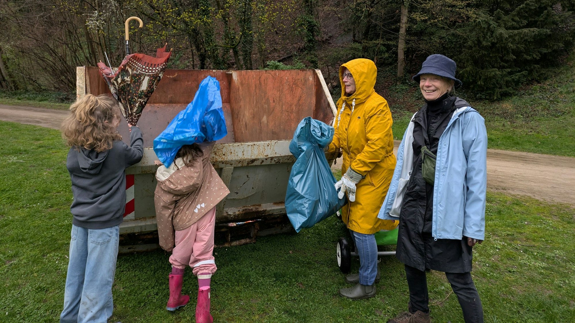 Zwei Erwachsene und zwei Kinder werfen Müll in einen Container.