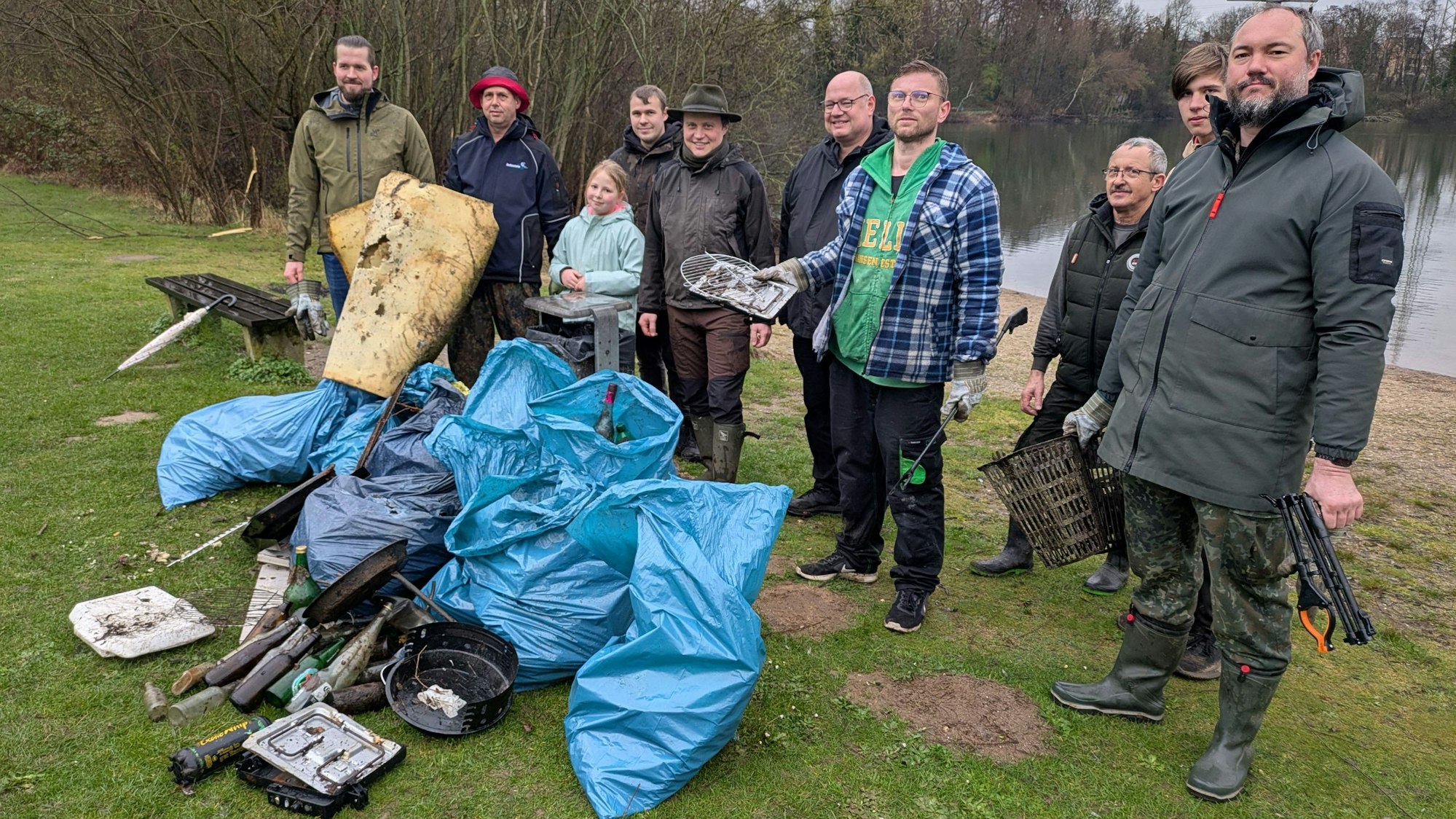 Männer und ein Kind stehen vor Müllsäcken an einem Seeufer.