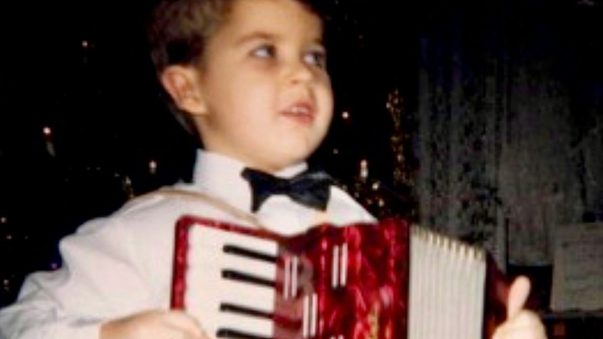 En Kind in weißem Hemd und mit Fliege spielt Akkordeon.