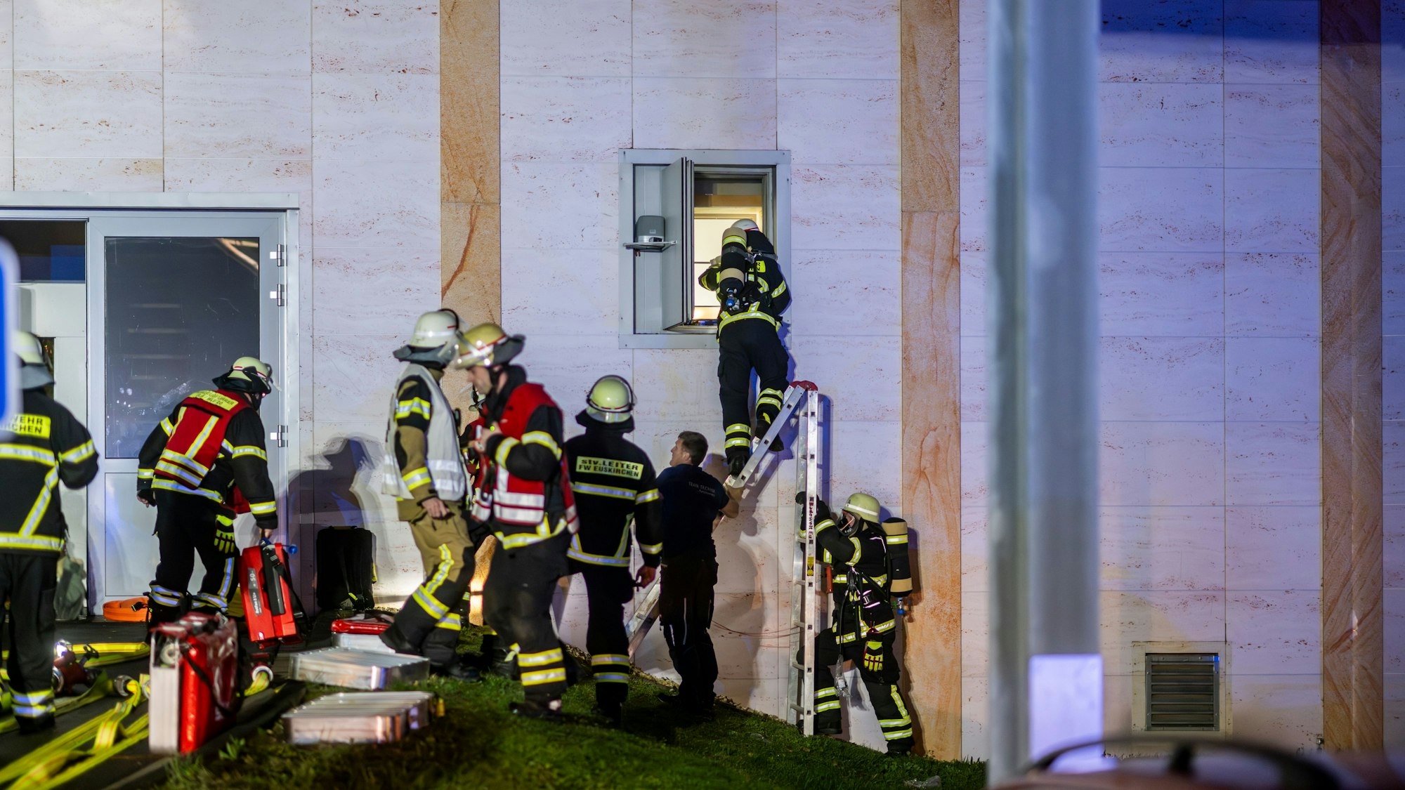 Feuerwehrleute steigen über eine Leiter durch ein Fenster in ein Gebäude.