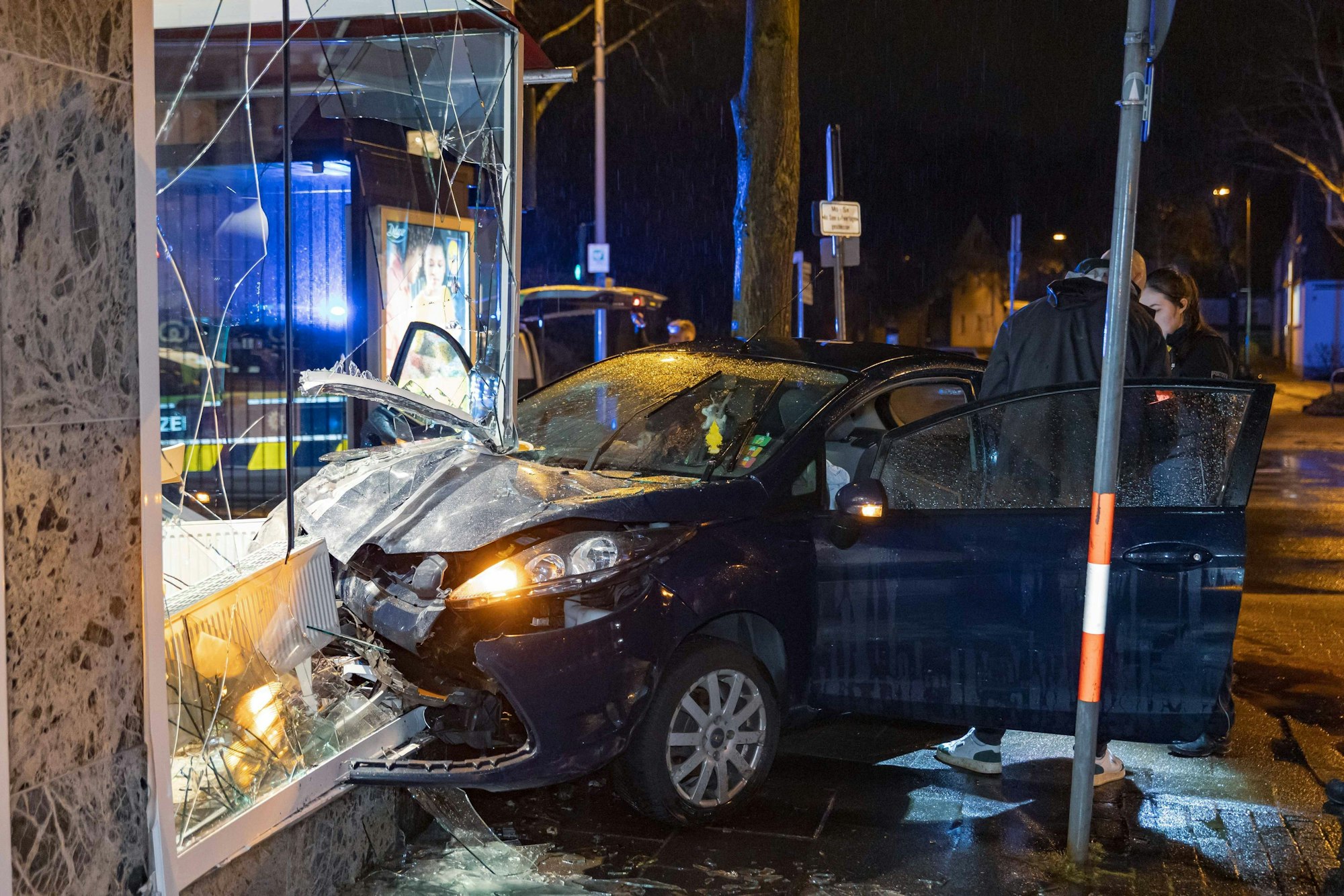 Ermittler stehen an der Unfallstelle, wo ein Fahrer mit seinem Auto in ein Schaufenster gekracht ist.