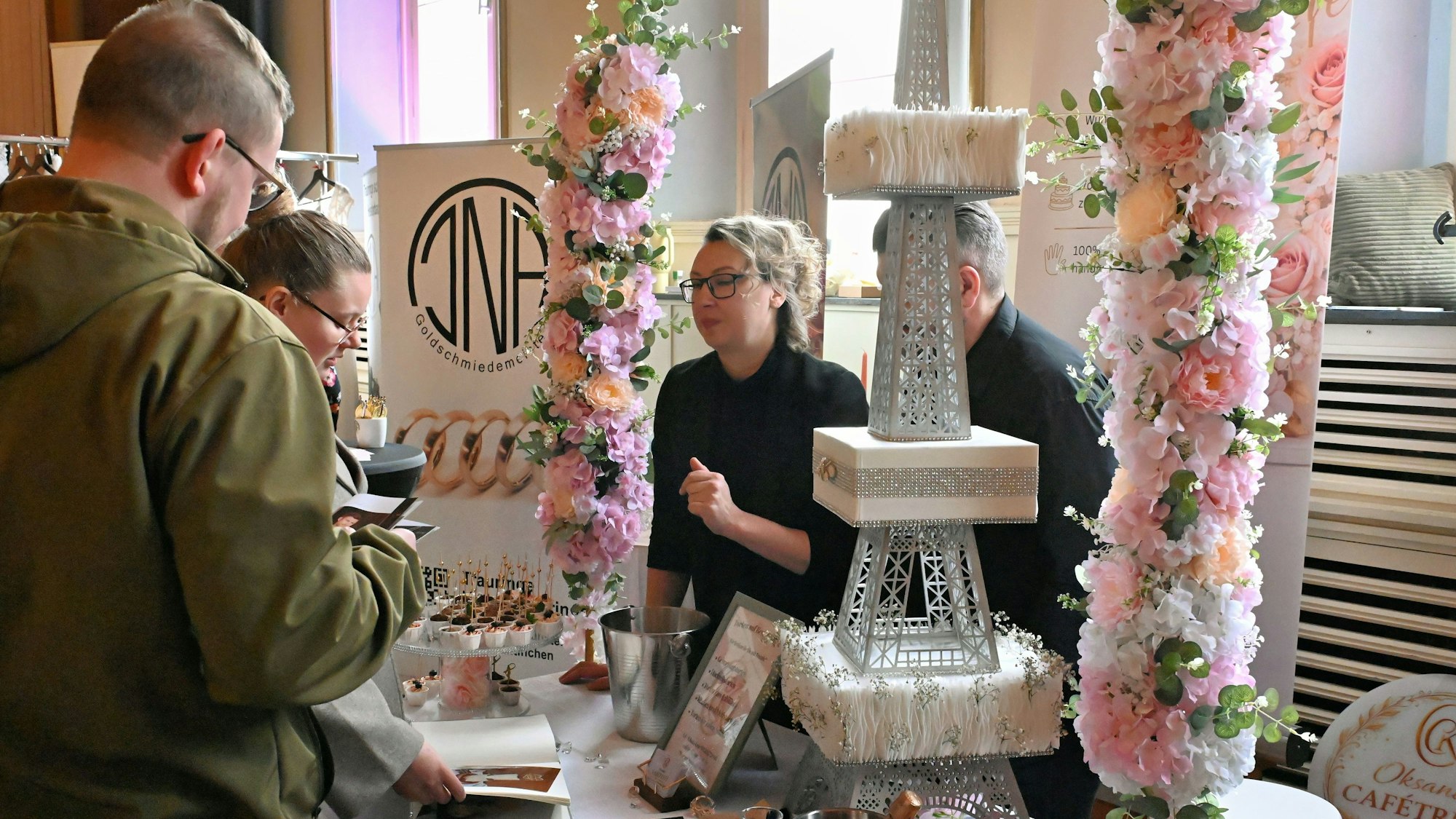 Ein Paar steht an einem Stand mit einer Hochzeitstorte im Stil des Eiffelturms.