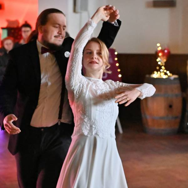 Eine Frau im Brautkleid und ein Mann im schwarzen Anzug tanzen zusammen.