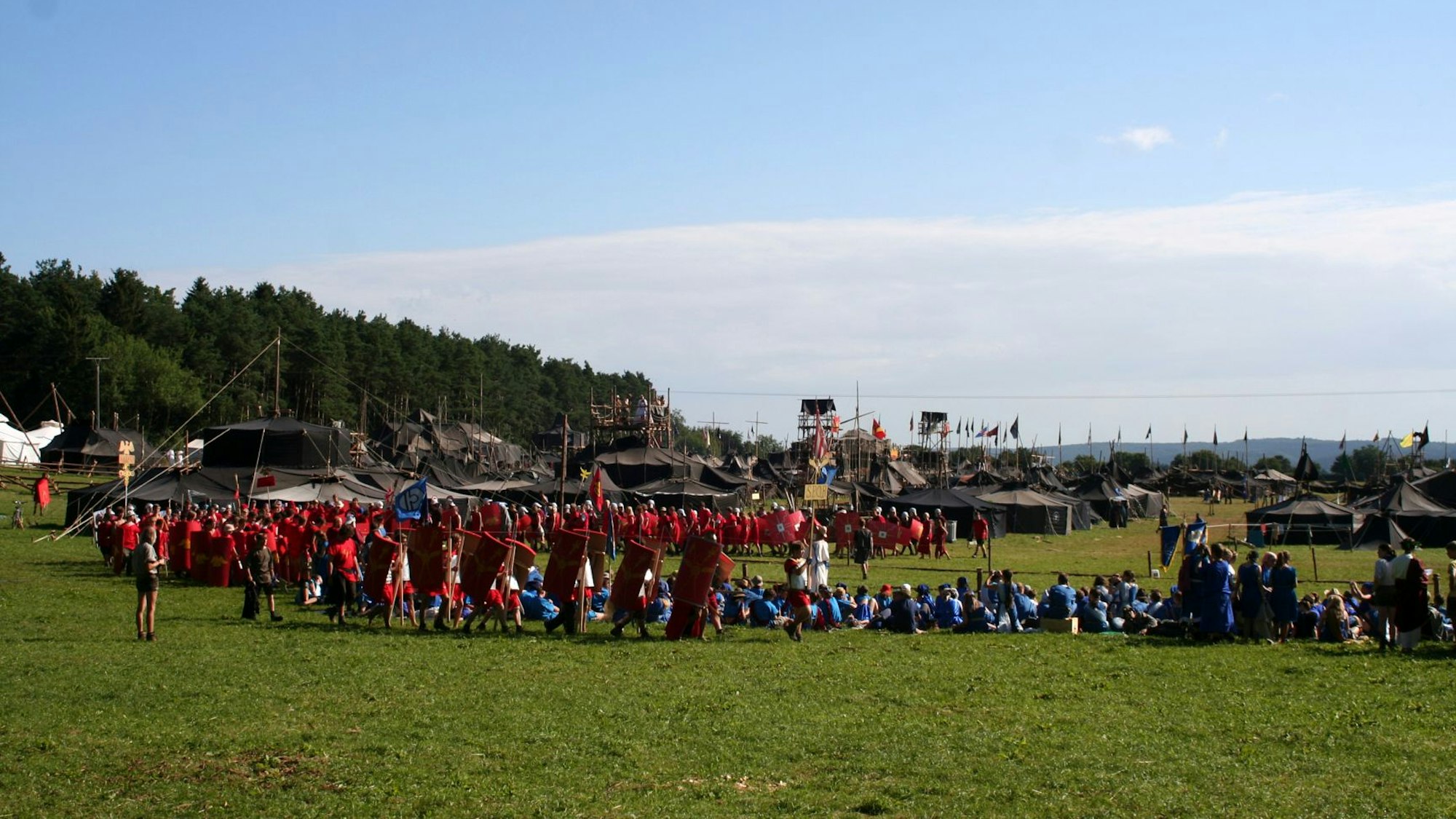 Die Teilnehmer stehen auf einer Wiese, im Hintergrund sind große schwarze Zelte zu sehen.